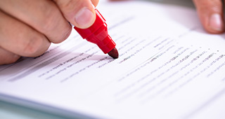 Hand markiert Text auf einem Dokument mit rotem Filzstift, Fokus auf Filzstift und Textzeilen.